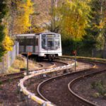 Moderne tog på buede spor omgitt av høsttrær med gyllent løvverk, som skaper et pittoresk landskap med offentlig transport.