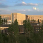 Arkitektillustrasjon av det planlagte Mjøssykehuset i Moelv, med lyse fasader omgitt av skog.